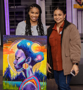 Two women standing behind a colorful painting.