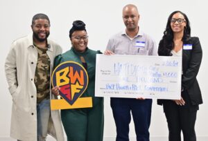 Four people standing together, holding a giant check