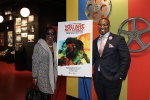 People standing next to a documentary poster in a theater.