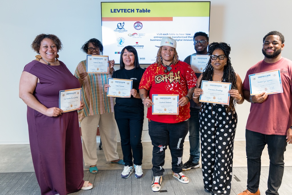 A group holding certificates stands in front of a tv.